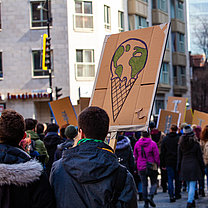 Eine Demonstration zieht durch eine Straße, die Teilnehmenden halten selbstgestaltete Plakate hoch.